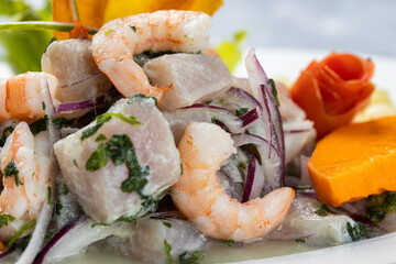 Close up shot of a white fish and shrimp ceviche, served on a white plate, isolated against a rustic rustic gray wood background.