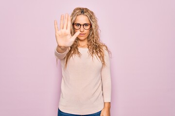 Young beautiful blonde woman wearing casual sweater and glasses over pink background doing stop...