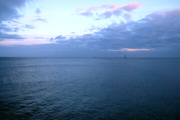 Fototapeta premium View of an outer harbor with ships anchored in far distance. Darkening sky with dramatic clouds, dark blue sea surface.