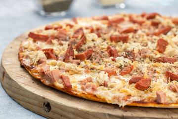 Bacon pizza, salami, made in a wood oven. Served on a rustic wooden board, placed on a rustic gray wooden background.