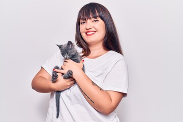 Young beautiful plus size woman smilling happy and confident. Standing with smile on face holding adorable cat over isolated white background