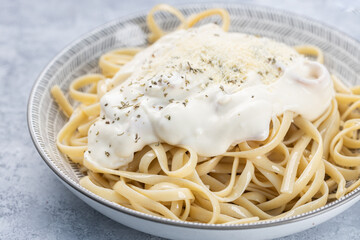 Close up of plate of pasta a la carbonara with parmesan cheese, served on a rustic textured plate, on a rustic wooden background.