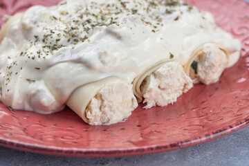 Plate of cannelloni stuffed with ricotta served with bechamel sauce on a rustic plate on a gray wooden background.