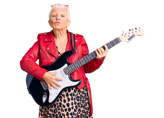 Fototapeta premium Senior beautiful woman with blue eyes and grey hair wearing a modern look playing electric guitar looking at the camera blowing a kiss on air being lovely and sexy. love expression.