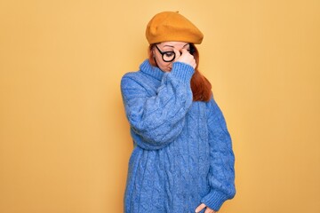 Obraz premium Young beautiful redhead woman wearing french beret and glasses over yellow background tired rubbing nose and eyes feeling fatigue and headache. Stress and frustration concept.