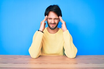 Handsome hispanic man wearing casual sweater sitting on the table suffering from headache desperate and stressed because pain and migraine. hands on head.