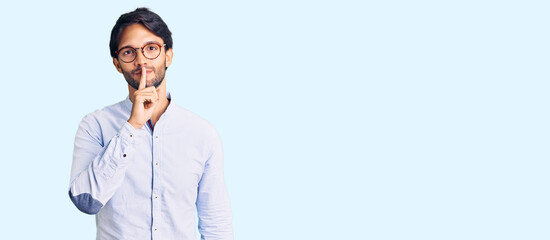 Handsome hispanic man wearing business shirt and glasses asking to be quiet with finger on lips....