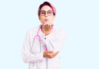 Young beautiful woman with pink hair wearing doctor uniform looking at the camera blowing a kiss...