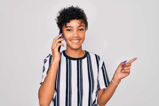 Young beautiful african american afro woman having conversation talking on the smartphone very happy pointing with hand and finger to the side