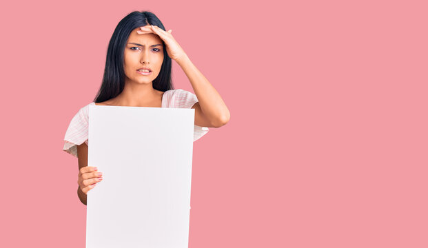 Young beautiful latin girl holding blank empty banner stressed and frustrated with hand on head, surprised and angry face