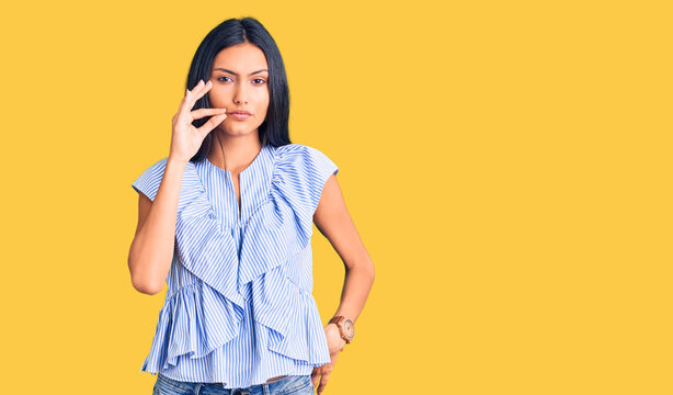 Young beautiful latin girl wearing casual clothes mouth and lips shut as zip with fingers. secret and silent, taboo talking