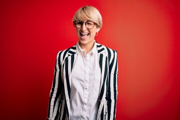 Blonde business woman with short hair wearing glasses and striped jacket over red background...
