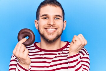 Naklejka premium Young handsome man hoding donut screaming proud, celebrating victory and success very excited with raised arm