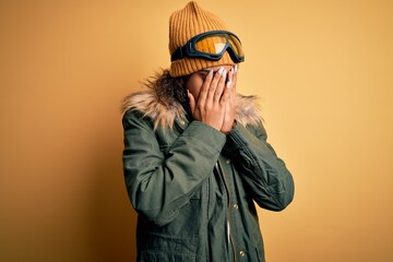 Young african american afro skier girl wearing snow sportswear and ski goggles with sad expression covering face with hands while crying. Depression concept.