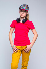 Youth Lifestyle. Portrait of Tranquil Caucasian Teenage Girl with Wireless Headphones. Posing in Colorful Cap Over Gray Background.