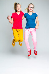 Youth Lifestyle. Full Length Portrait of Two Jumping Teenage Sisters In Colorful Clotinhg. Posing...