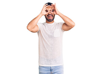 Fototapeta premium Young hispanic man wearing casual clothes doing ok gesture like binoculars sticking tongue out, eyes looking through fingers. crazy expression.