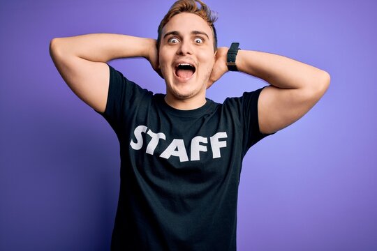 Young handsome redhead worker man wearing staff t-shirt uniform over purple background Crazy and scared with hands on head, afraid and surprised of shock with open mouth