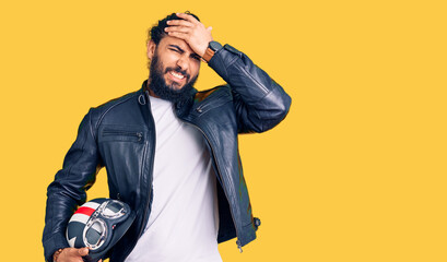 Young arab man holding motorcycle helmet stressed and frustrated with hand on head, surprised and...