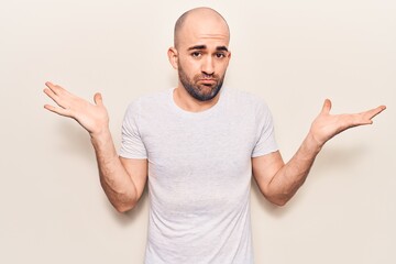 Young handsome bald man wearing casual t shirt clueless and confused with open arms, no idea and doubtful face.