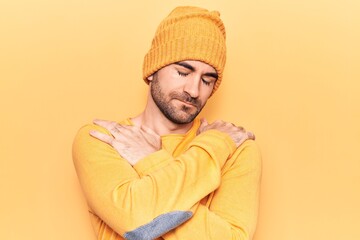 Young handsome bald man wearing sweater and wool cap hugging oneself happy and positive, smiling confident. self love and self care