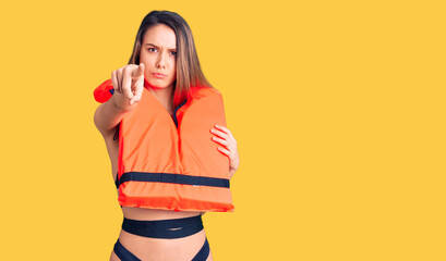 Young beautiful girl wearing life jacket pointing with finger to the camera and to you, confident gesture looking serious