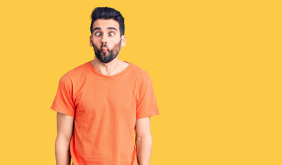 Young handsome man with beard wearing casual t-shirt making fish face with lips, crazy and comical gesture. funny expression.