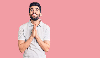 Young handsome man with beard wearing casual polo begging and praying with hands together with hope expression on face very emotional and worried. begging.