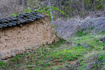 Mud brick wall with black tile roof in wooded area