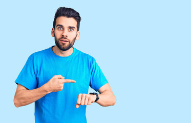 Young handsome man with beard wearing casual t-shirt in hurry pointing to watch time, impatience,...