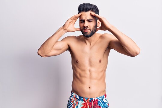 Young handsome man with beard shirtless wearing swimwear with hand on head, headache because stress. suffering migraine.