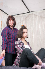 Obraz premium A woman twists a girl's hair into curlers at home on the bed