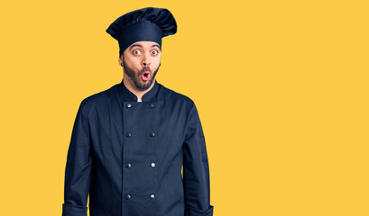 Young hispanic man wearing cooker uniform afraid and shocked with surprise expression, fear and...