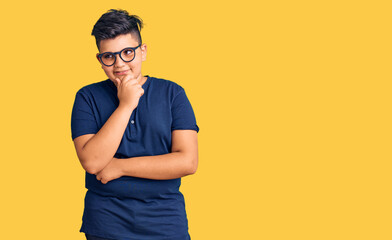 Little boy kid wearing casual clothes and glasses with hand on chin thinking about question, pensive expression. smiling with thoughtful face. doubt concept.