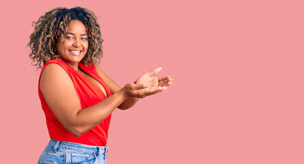 Young african american plus size woman wearing casual style with sleeveless shirt pointing aside with hands open palms showing copy space, presenting advertisement smiling excited happy