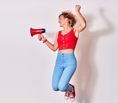 Young beautiful caucasian woman screaming using megaphone. Jumping over isolated white background