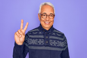 Naklejka premium Middle age senior grey-haired man wearing glasses and winter sweater over purple background showing and pointing up with fingers number two while smiling confident and happy.