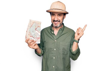 Middle age handsome tourist man on vacation wearing explorer hat holding city map smiling happy pointing with hand and finger to the side