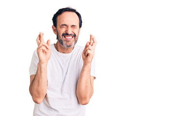 Middle age handsome man wearing casual t-shirt gesturing finger crossed smiling with hope and eyes closed. luck and superstitious concept.