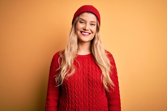Young beautiful blonde woman wearing casual sweater and wool cap over white background with a happy and cool smile on face. Lucky person.