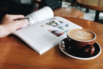 Close-up view of latte coffee and magazines placed on a wooden table in a coffee shop
