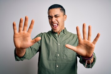 Young brazilian man wearing casual shirt standing over isolated white background showing and pointing up with fingers number ten while smiling confident and happy. - obrazy, fototapety, plakaty