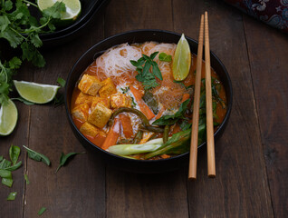 Thai vegan red curry woth tofu, noodles, beans and carrots on wooden table, copy space
