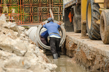 Workers control to put concrete pipe in groove - obrazy, fototapety, plakaty