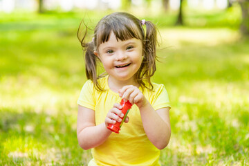 Portrait of a laughing girl with syndrome down blowing bubbles in a summer park