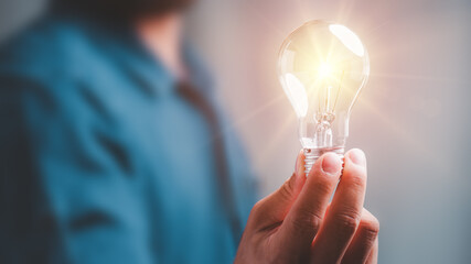 Idea innovation and inspiration concept.Hand of man holding illuminated light bulb, concept creativity with bulbs that shine glitter.Inspiration of ideas for sustainable business development. - obrazy, fototapety, plakaty
