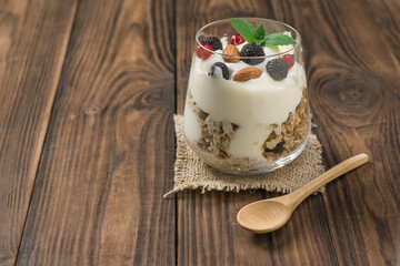 Yogurt, granola and berries in a glass and a wooden spoon on a wooden table.