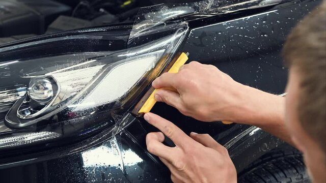 Paint protection film Installation on a black car. Master applies polyurethane protective film using squeegee tool to remove excess water from under the film surface.