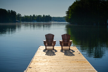 Two Adirondack chairs on a wooden dock overlooking a calm lake in Ontario cottage country....