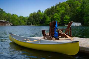 Two Adirondack chairs on a wooden dock facing the blue water of a lake in Muskoka, Ontario Canada....